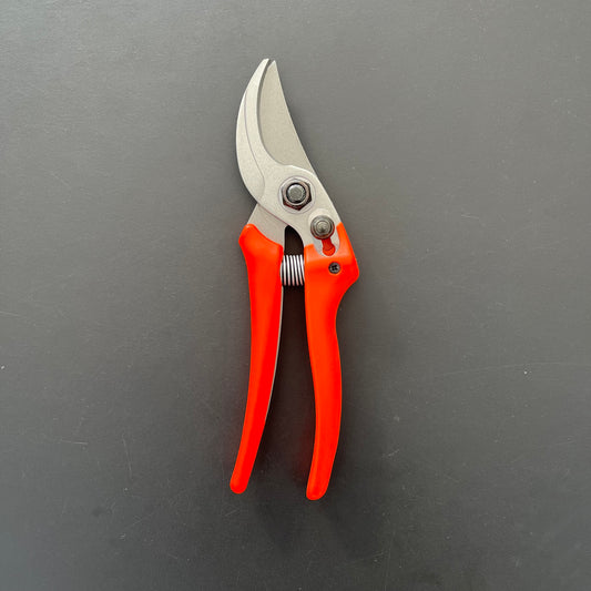 Eine Gartenschere Löwe Original Löwe 14 – Economic Clean Cut mit leuchtend roten Griffen und silberner Klinge auf einer dunkelgrauen Oberfläche – ideal für präzise Gartenarbeiten.