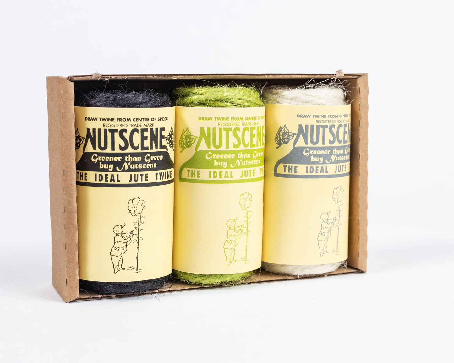 Das Nutscene Twines Ltd Mini Reels of Twine 3er-Pack enthält schwarze, grüne und natürliche Schnüre (jeweils 42 Fuß), verpackt in einer braunen Schachtel. Jede biologisch abbaubare Spule hat ein gelbes Etikett mit schwarzem Text und der Abbildung einer Person, die einen Luftballon hält.