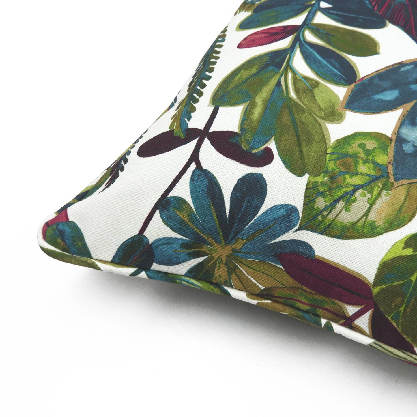 Eine Nahaufnahme des Riva Home – Tonga Kissen Jewel zeigt einen lebendigen botanischen Druck mit grünen, blauen und burgunderfarbenen Blättern auf Weiß, akzentuiert durch einen kontrastierenden Paspelrand für zusätzliche Eleganz.