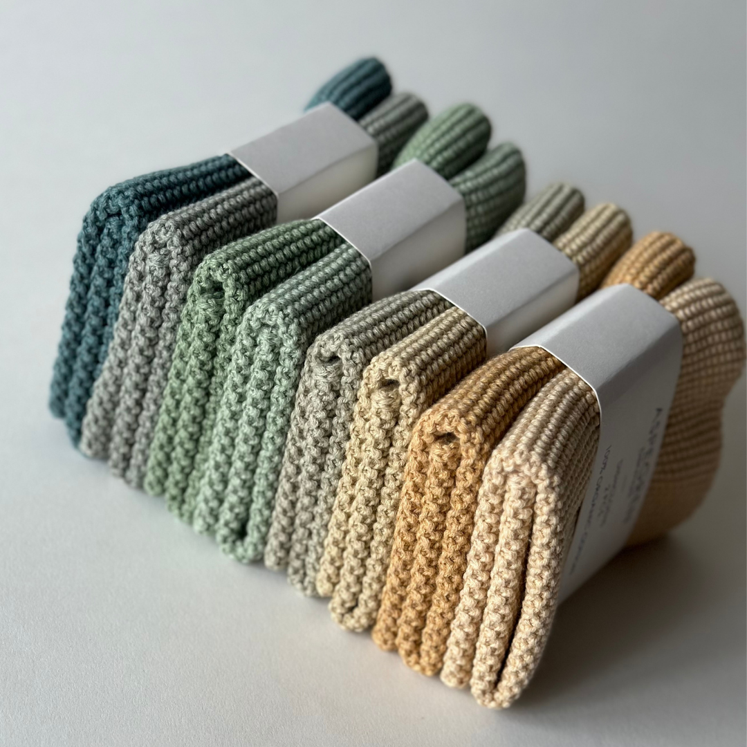 Vier Sätze Aspegren Denmark Spültücher, gestrickt und einfarbig in Gold, sind ordentlich gefaltet und jeweils mit einem weißen Papierband umwickelt auf einer hellen Fläche gestapelt.