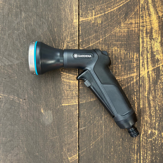 Eine schwarze Gardena Eco Line Bewässerungsbrause von Gardena aus recyceltem Kunststoff mit blauem Ring ruht auf einer dunklen Holzoberfläche, die von gelblichen Kratzern und sichtbarer Maserung gekennzeichnet ist.