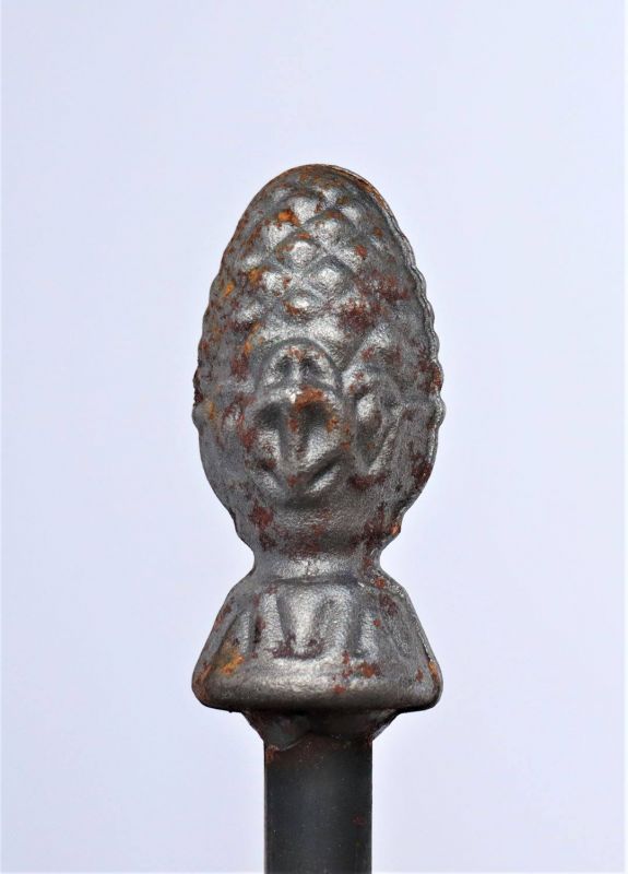 Eine Nahaufnahme des Hirsch-Laternenstabs "Bino Pinie" mit 2-fachem Fuß zeigt das strukturierte, metallische Ornament in Form eines Pinienzapfens mit etwas Rost, das auf der zylindrischen Stange angebracht ist, vor einem schlichten hellen Hintergrund.