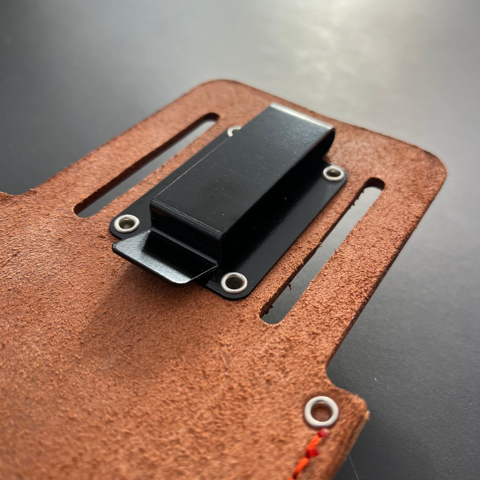 Nahaufnahme des Löwe Original Löwe - Lederholster für Gartenscheren, mit einem schwarzen Metallclip, der mit Nieten befestigt ist, und einer detaillierten Ledertextur und -nähten. Der dunkle, glatte Hintergrund unterstreicht dieses hochwertige Gartengeräteholster von Löwe.