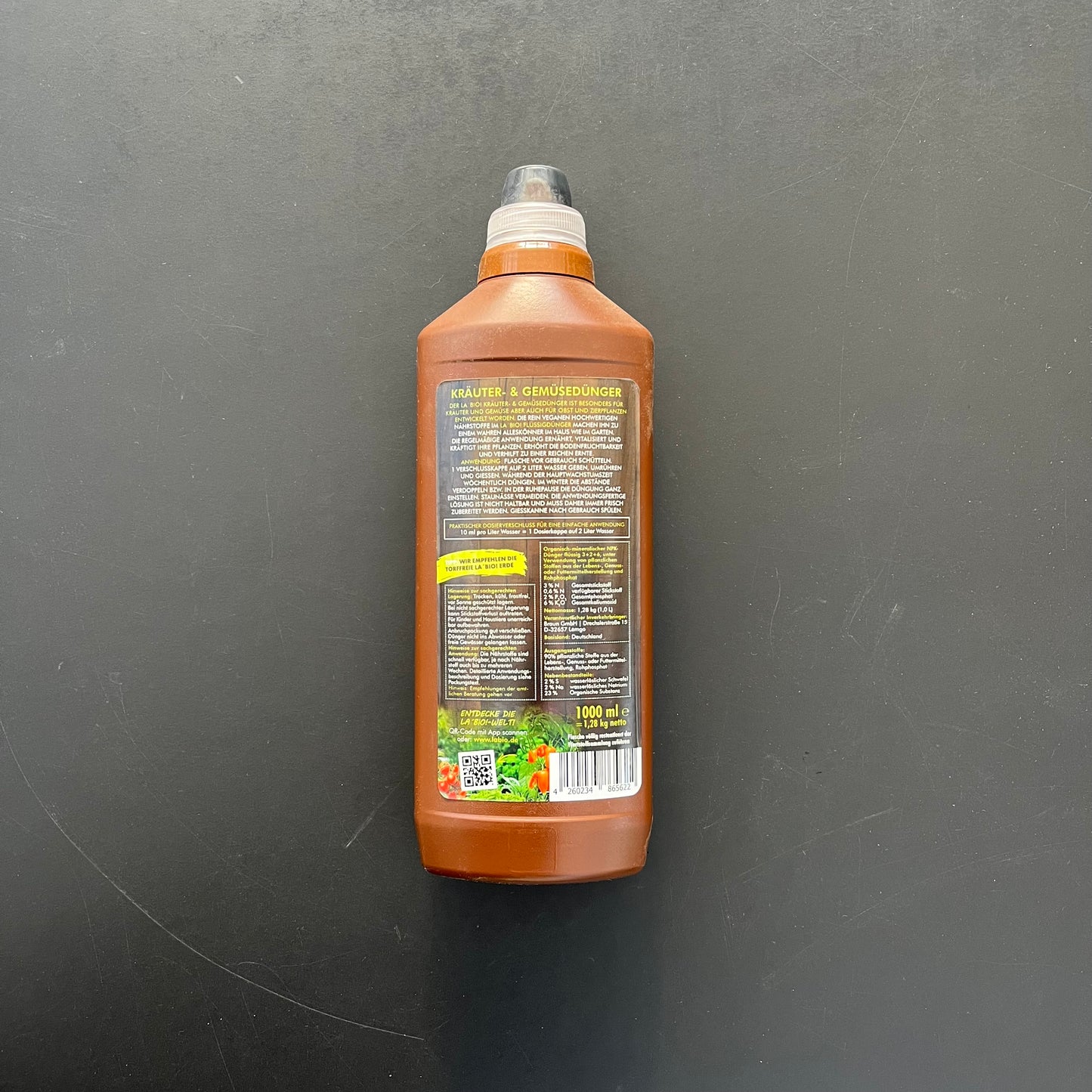 Der LaBio Kräuter & Gemüsedünger kommt in einer braunen Plastikflasche mit schwarzem Verschluss und einem meist deutschen Etikett mit Gemüse und Kräutern. Es ist ein biologischer Dünger, der Ihren Pflanzenertrag steigern soll.