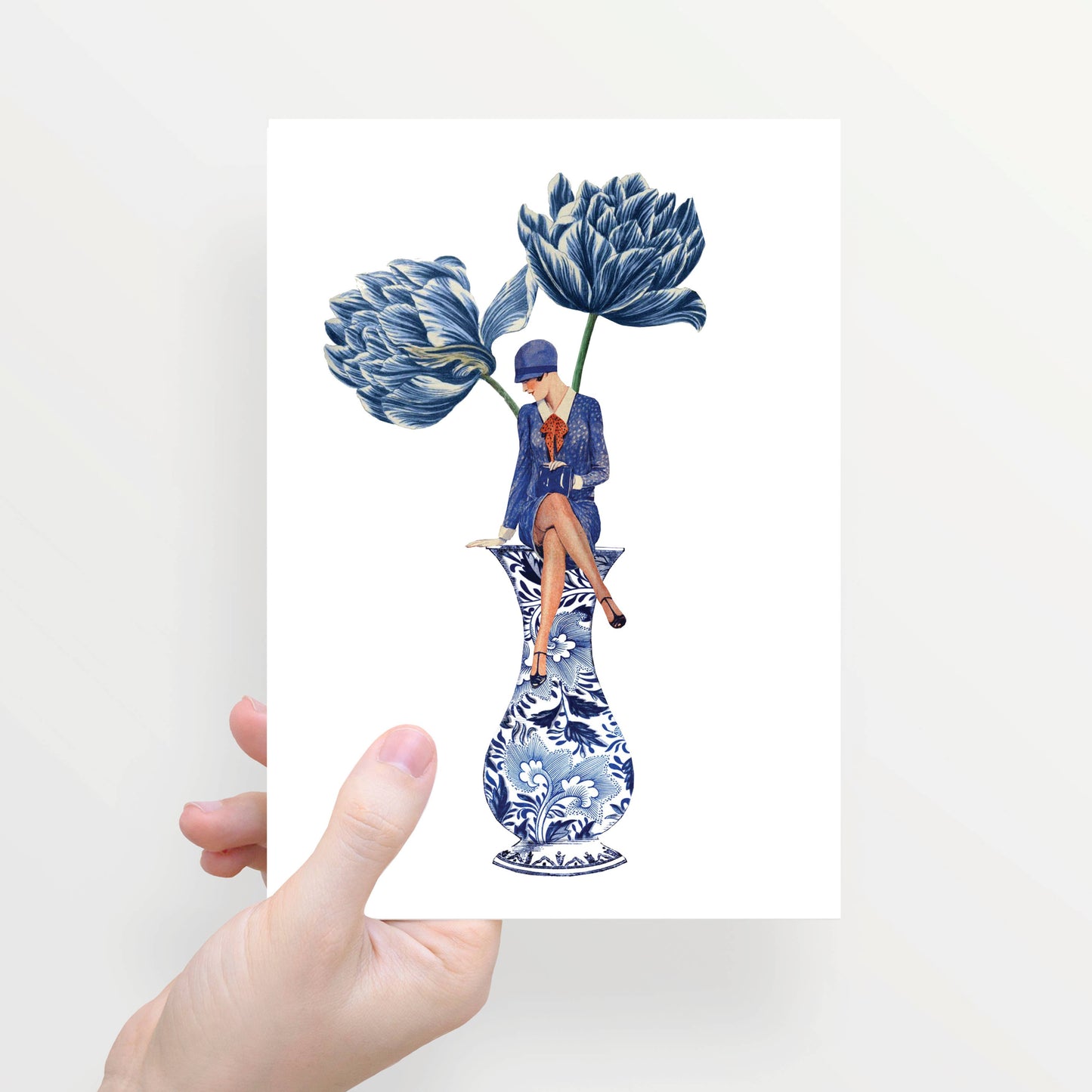 Eine Hand hält die Lylies Grußkarte: Zur Hälfte gefaltet, mit Damenumschlag auf einer blauen Vase und zwei großen blauen Blumen im Hintergrund.