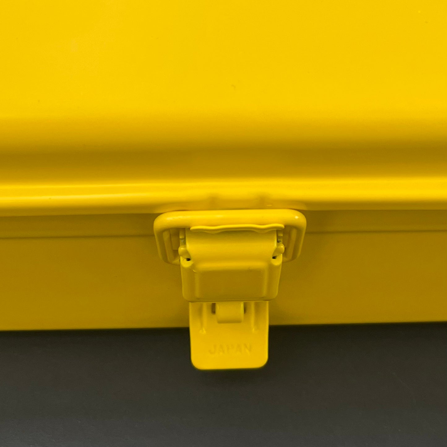Nahaufnahme des gelben Verschlusses einer Niwaki Y-Type Toolbox von Niwaki mit der Prägung "JAPAN". Ein dunkler Hintergrund hebt den Riegel hervor - ein funktionelles Detail, das ideal für die effiziente Organisation von Gartengeräten ist.