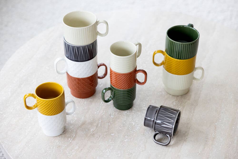 Fünf Stapel bunter Sagaform GmbH Coffee & More Teetasse, 2-tlg.-Keramikbecher mit Strukturmuster stehen auf einer hellen Tischplatte, während ein grauer Becher auf der Seite liegt. Die Farben sind gelb, weiß, grün, orange und grau.