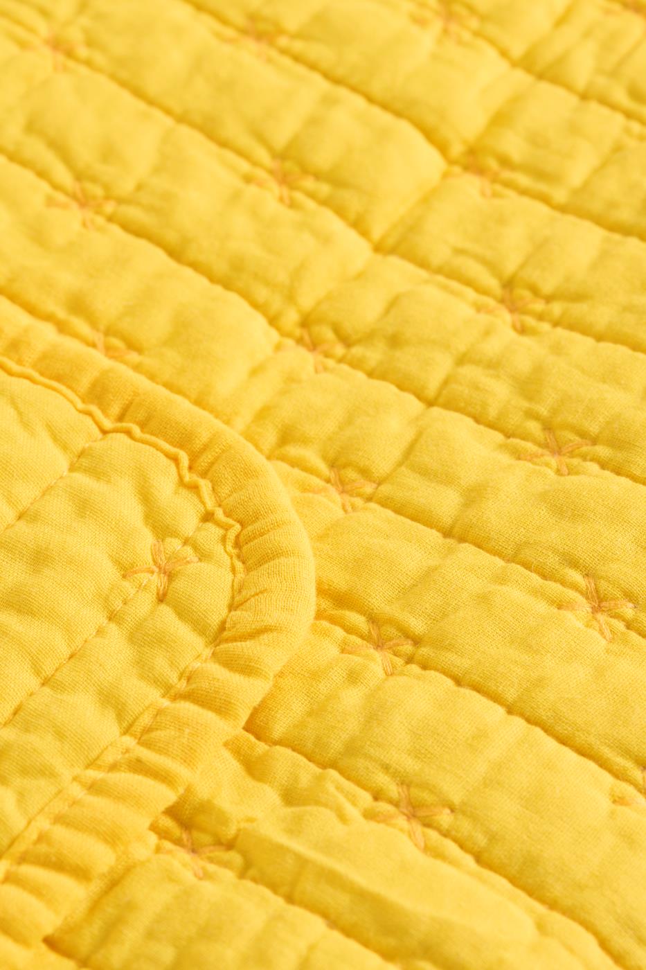 Nahaufnahme der Ib Laursen | Quilt Decke gelb mit Kreuzstich von IB Laursen, mit leuchtend gelbem Stoff, sichtbaren Kreuzstichen, einem Gittermuster, abgerundeten Ecken und einer weichen, strukturierten Oberfläche.