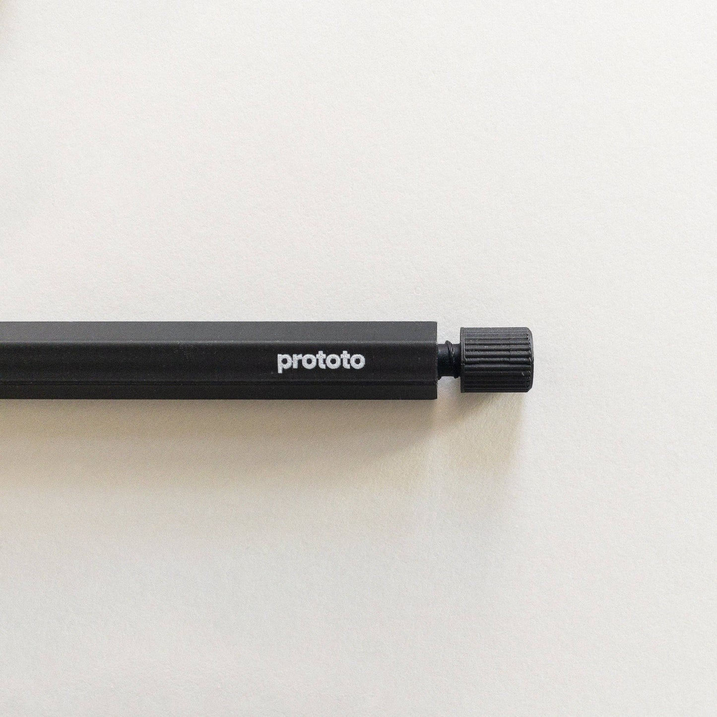 Ein schwarzer Prototo Zero Waste Kugelschreiber mit der Aufschrift „Prototo“ in Weiß und einem strukturierten Drehknopf aus klimaneutralem, erdölfreiem Bioplastik liegt auf einer cremefarbenen Oberfläche, wobei nur ein Teil des Stifts sichtbar ist.