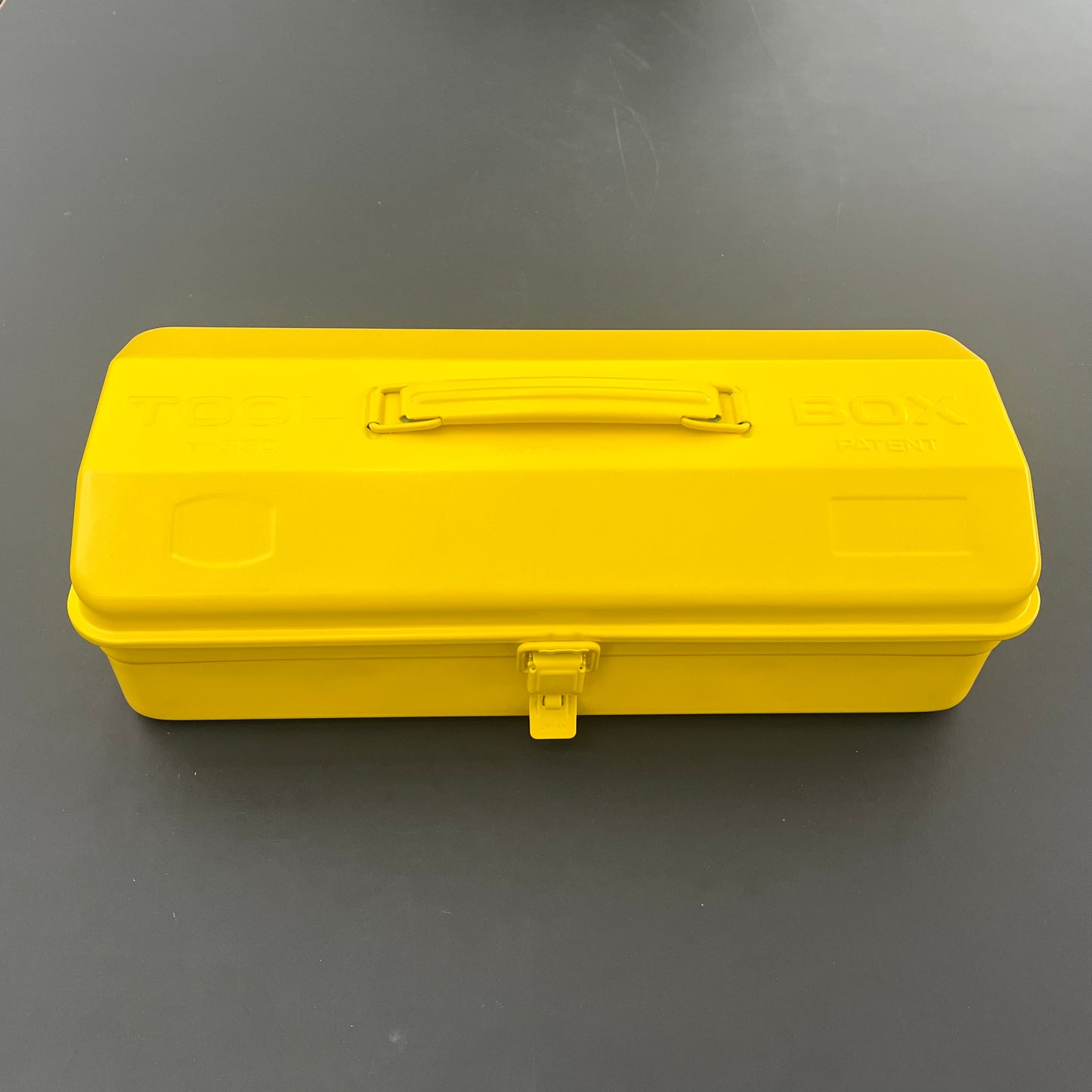 Die leuchtend gelbe Niwaki Y-Type Toolbox mit stabilem Griff und sicherem Verschluss ruht geschlossen auf einer dunkelgrauen Oberfläche und eignet sich perfekt für die Organisation Ihres Gartenbedarfs.