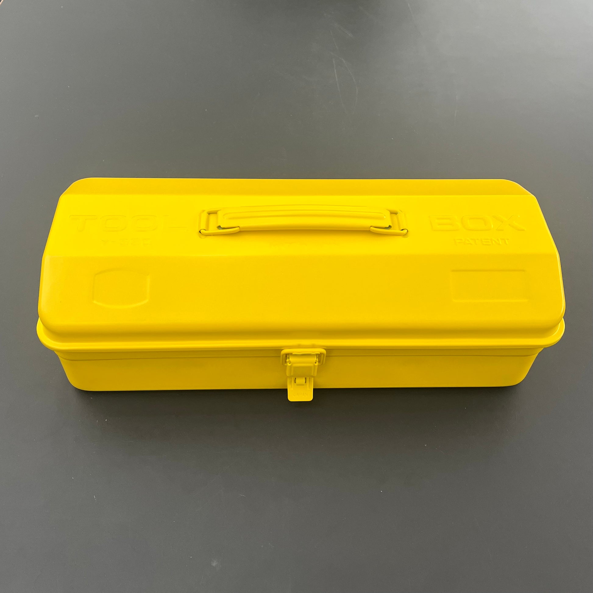 Die leuchtend gelbe Niwaki Y-Type Toolbox mit stabilem Griff und sicherem Verschluss ruht geschlossen auf einer dunkelgrauen Oberfläche und eignet sich perfekt für die Organisation Ihres Gartenbedarfs.