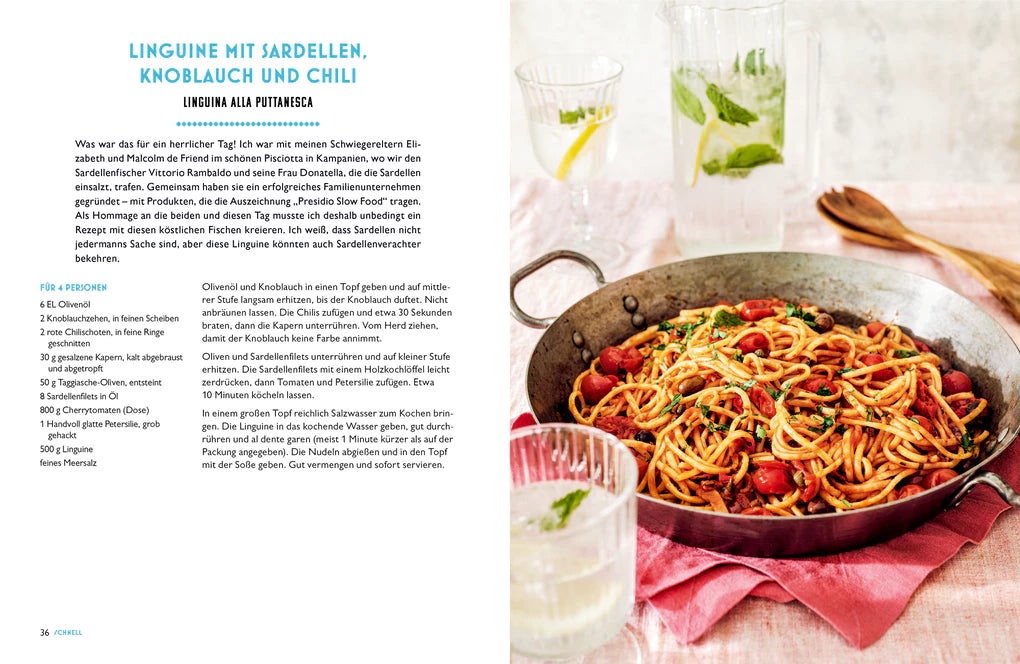 Ein Teller Linguine mit Sardinen, Kirschtomaten und Kräutern steht auf einem Holztisch, daneben Gläser mit Wasser und Besteck. Links steht ein Rezept aus Ginos italienische Küche vom Hölker Verlag, das von italienischen Familiengerichten inspiriert ist.
