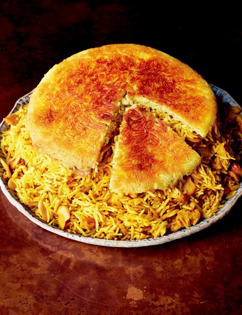 Eine große Platte mit goldgelbem persischem Tahchin, inspiriert von Rezepten aus der "Gewürzküche" des Hölker Verlags - ein gebackenes Reisgericht mit einer knusprigen Safrankruste, bei dem eine Scheibe abgeschnitten wird, um den gelben Reis und das Huhn im Inneren zu enthüllen.