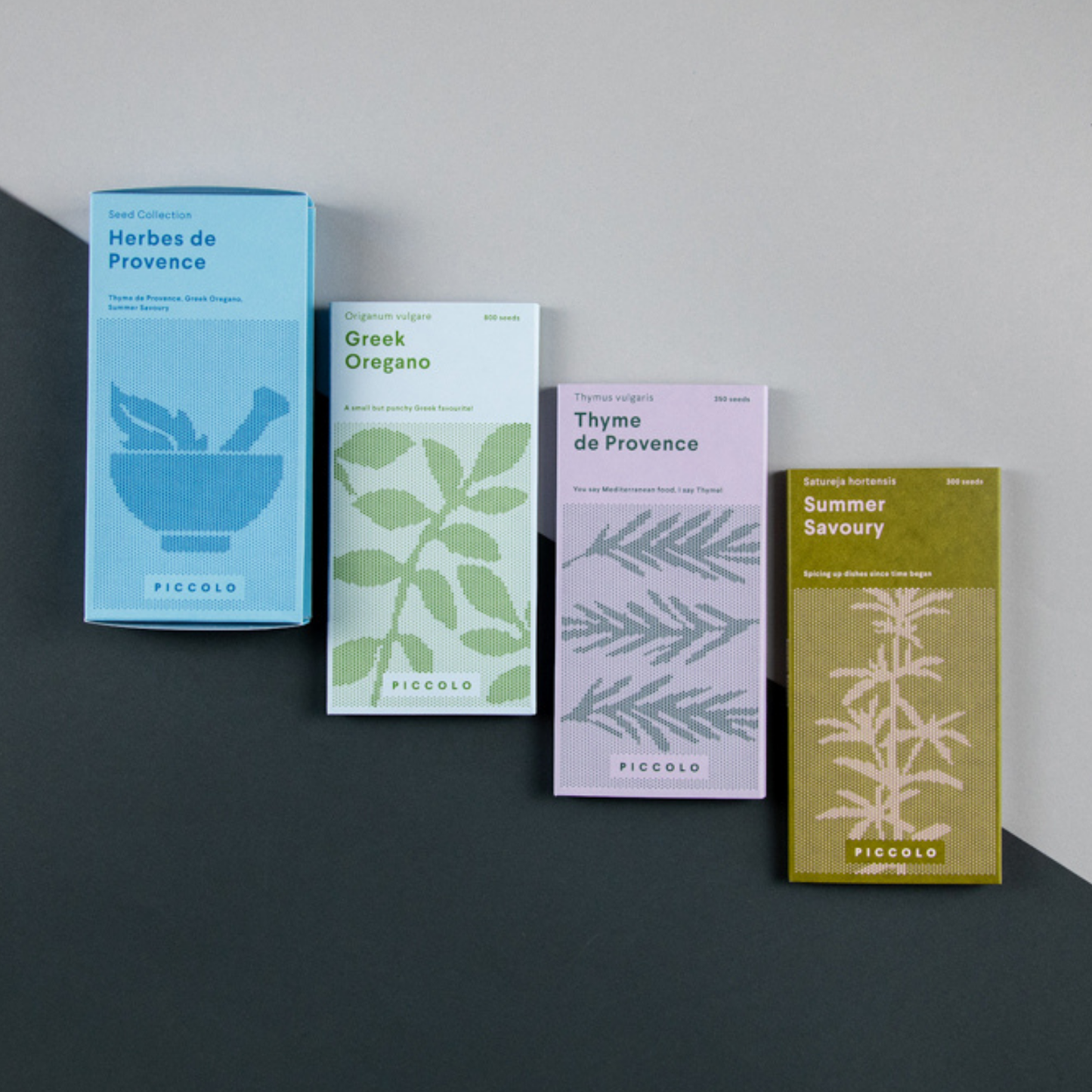 Vier bunte Päckchen „Piccolo Seeds – Kräuter der Provence“ – in Blau, Grün, Lavendel und Gelb – sind auf einem dunklen Untergrund angeordnet. Jedes Päckchen ist mit minimalistischen Kräuterillustrationen und -namen versehen: Kräuter der Provence, Griechischer Oregano, Thymian und Bohnenkraut.