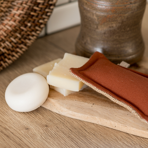 The Simple Things – Waschbarer Schwamm | Die Scharfen von Simple Things liegt auf einer Holzoberfläche neben handgefertigten französischen Seifen, einem braunen Keramikbehälter und einem rechteckigen rostfarbenen Beutel aus Baumwoll-/Jutegewebe.