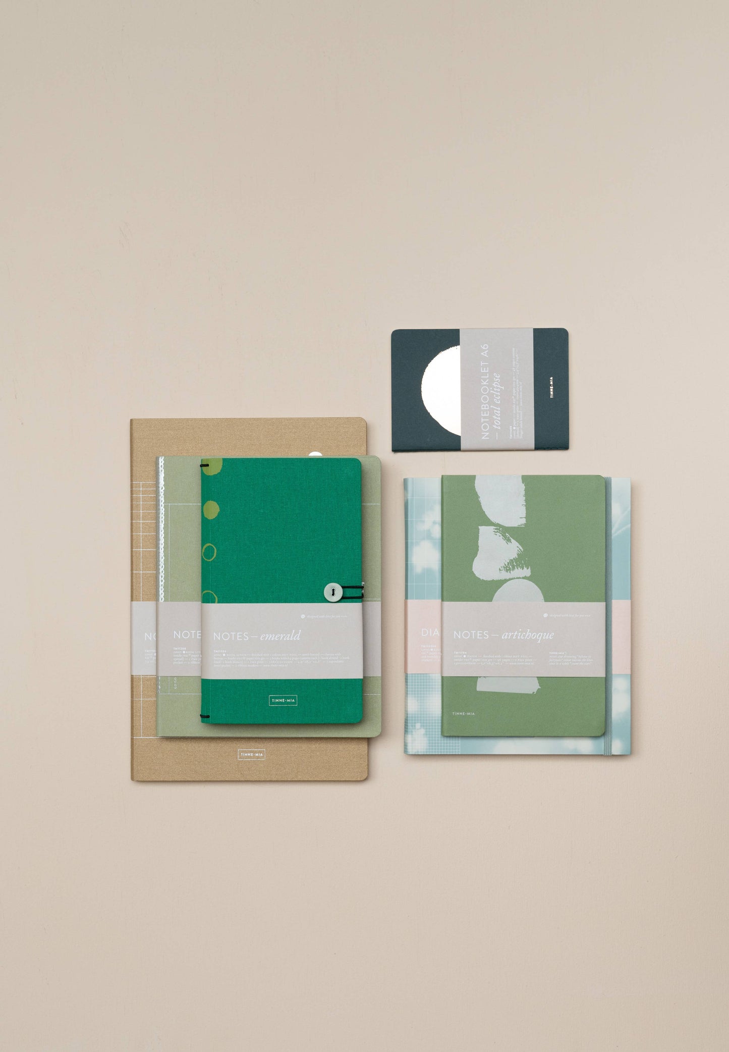 Ein Flat-Lay von vier Tinne Mia Notizbuch mit Knopf in Smaragd, FSC Mix zertifiziert, mit minimalistischen Leinen-Covern in Grün- und Brauntönen auf beigem Hintergrund - ideal als Bullet Journal oder Tagebuch.