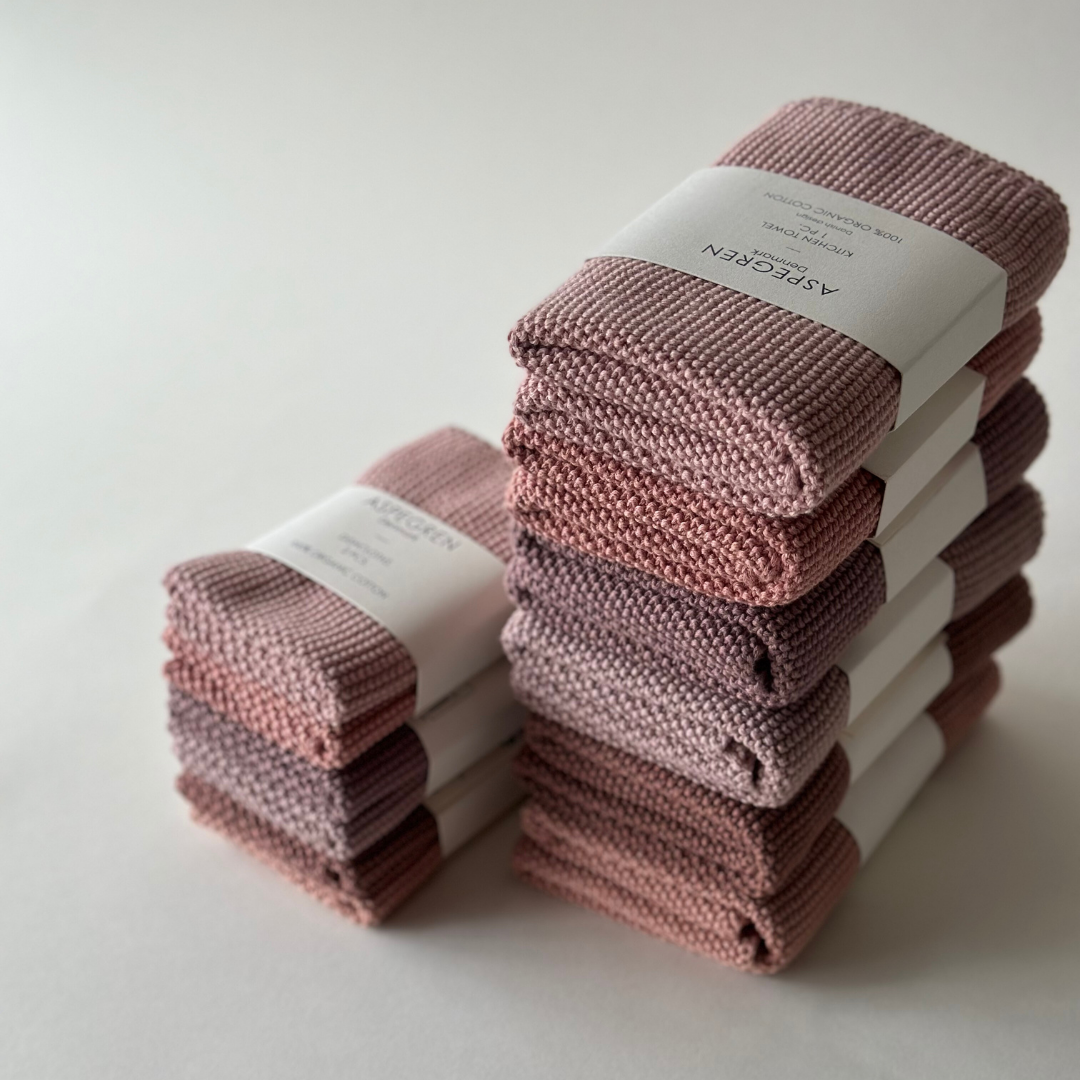 Zwei Stapel Aspegren Denmark - Küchentuch Solid in Pale Malve, jeweils mit weißem Papieretikett, sind auf einer weißen Fläche im sanften Licht arrangiert.