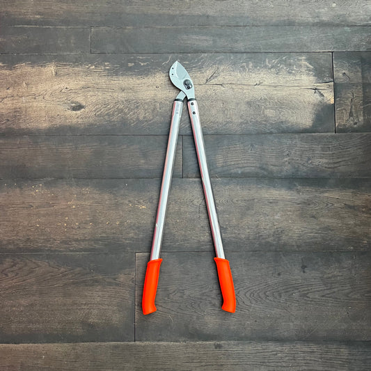 Die Löwe Astschere 22 (80 cm) von Löwe mit langen silbernen Stielen und orangefarbenen Griffen ruht auf einem dunklen Holzboden - perfekt für die präzise Gartenpflege.