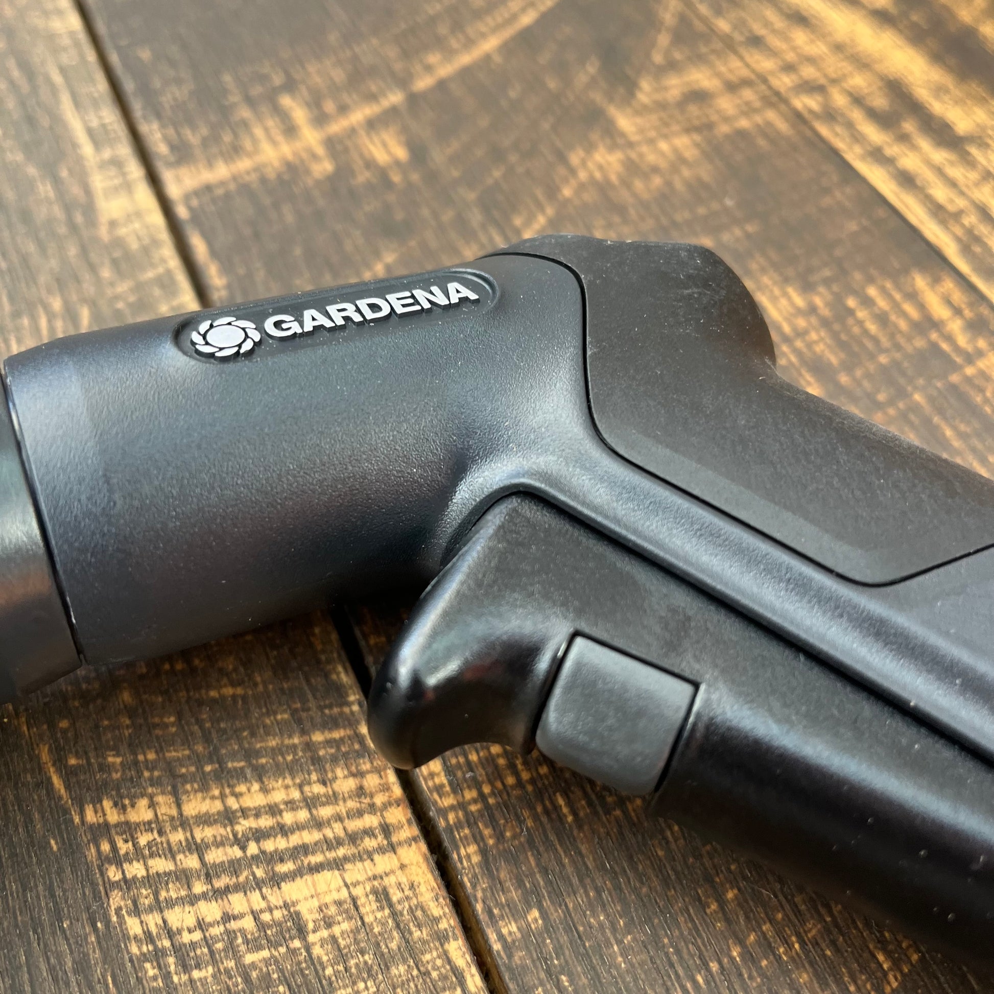 Nahaufnahme einer schwarzen Gardena Eco Line Bewässerungsbrause aus recyceltem Kunststoff von Gardena, die auf Holz aufliegt und das Markenlogo und die Griffdetails zeigt.