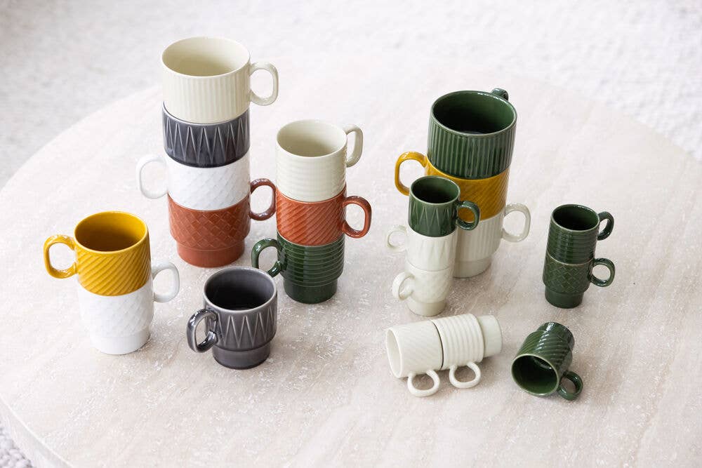 Ein Paar farbenfrohe Becher der Sagaform GmbH Coffee & More Teetasse (2-tlg.), gestapelt und arrangiert auf einem strukturierten runden Tisch, zeigen einzigartige Muster - perfekt für Ihre Lieblings-Kaffee- oder Tee-Momente.