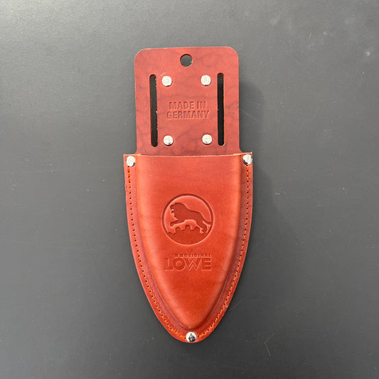 Das Original Löwe - Lederholster für Gartenscheren von Löwe ist mit einem Löwenlogo, "ORIGINAL LÖWE" und "MADE IN GERMANY" geprägt. Ausgestattet mit Metallnieten und Gurtschlitzen ist es ideal für Fans der Gartenarbeit. Abgebildet auf einer schwarzen Oberfläche.