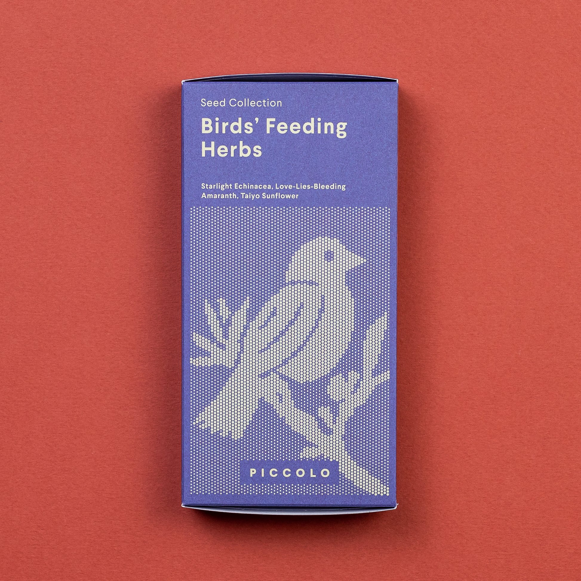 Eine lilafarbene Packung „Piccolo Seeds – Fütterungskräuter für Vögel“ mit einem Vogel auf einem Zweig auf rotbraunem Hintergrund. Die Packung enthält Kräuter für Wildvögel und trägt unten den Markennamen „Piccolo Seeds“.