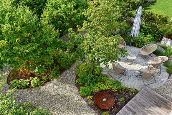 Luftaufnahme einer runden Terrasse mit Korbstühlen und Tisch - die perfekte Inspiration aus "Die schönsten Terrassen und Sitzplätze" vom Callwey Verlag für Ihren Traumgarten, umgeben von üppigem Grün, einem Kiesweg und einer Holzterrasse.
