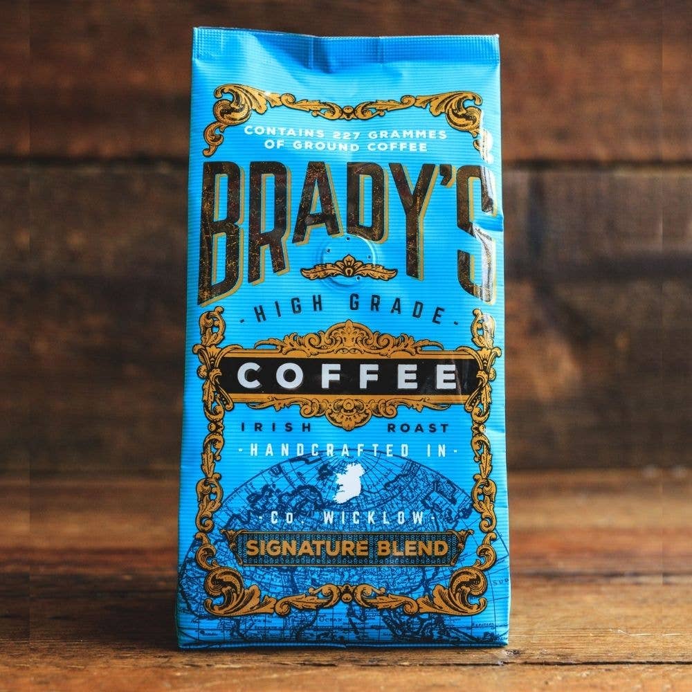 Eine blaue Tüte Brady's Coffee Company - Brady's Signature Blend Kaffee ist mit auffälligen goldenen und schwarzen Details versehen, die die hochwertige irische Röstung hervorheben, die von Brady's Coffee Company in der Grafschaft Wicklow vor einem hölzernen Hintergrund handgefertigt wird.