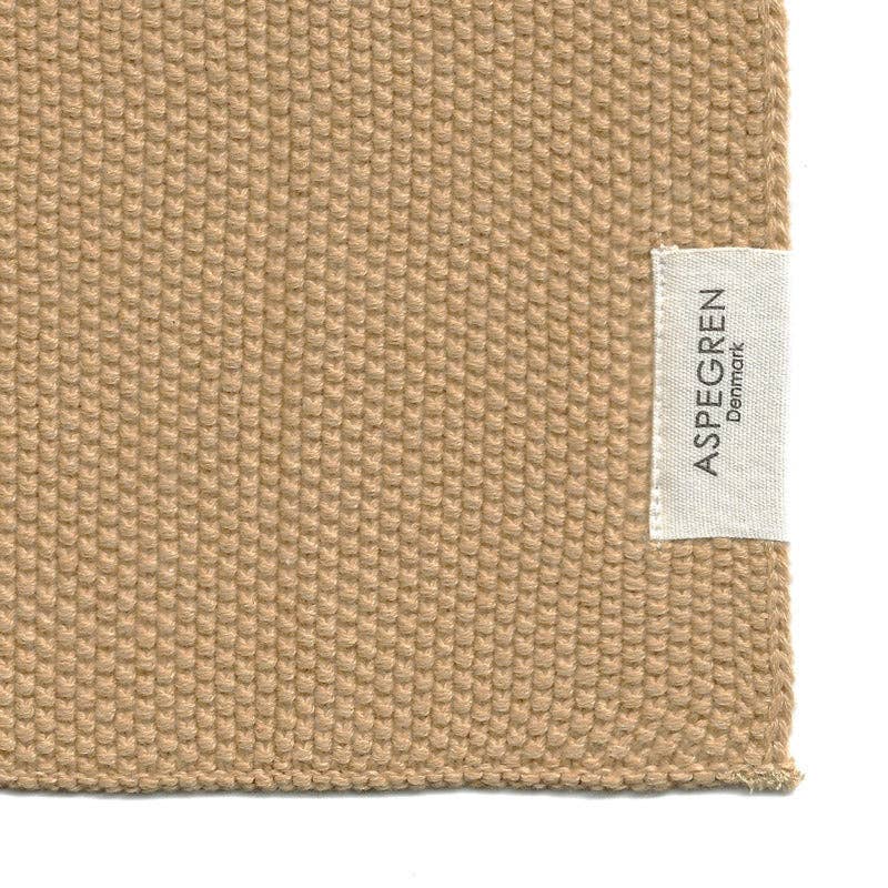 Eine Nahaufnahme der goldenen, strukturierten Spültücher aus gestrickter Bio-Baumwolle von Aspegren Denmark, mit einem kleinen weißen Etikett auf der rechten Seite mit dem Markennamen.