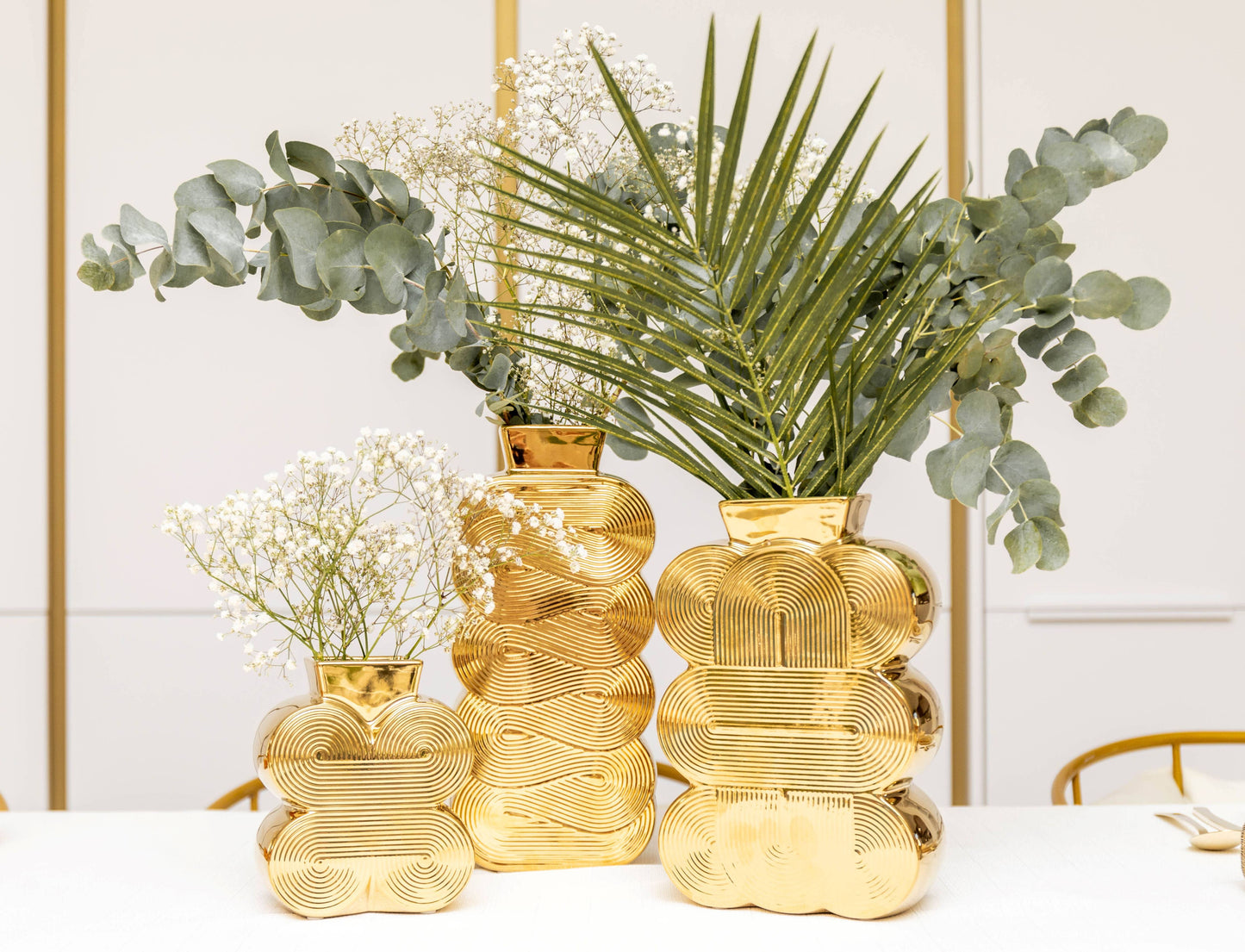 Die AULICA - BRILLANTGOLDVASE (16,5 x 7 x 25 cm) von AULICA besticht mit geometrischem Muster und glänzendem Gold – ideal für moderne Arrangements mit Grün und weißen Blumen im avantgardistischen Design.