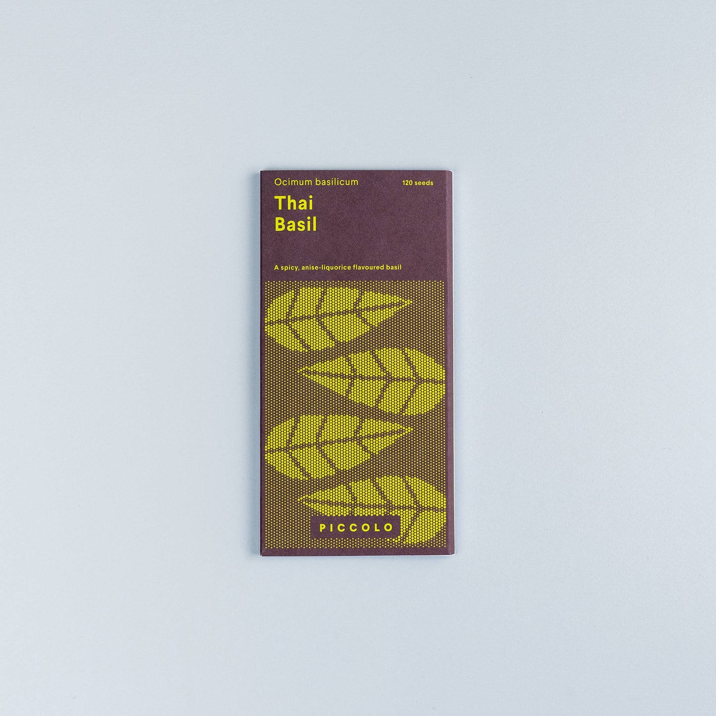 Ein Päckchen Piccolo Seeds - Basil Thai von Piccolo Seeds, mit stilisierten grünen Basilikumblättern und modernem gelben Text auf lila Hintergrund, fotografiert auf einer schlichten hellgrauen Oberfläche - ideal für Fans der asiatischen Küche.