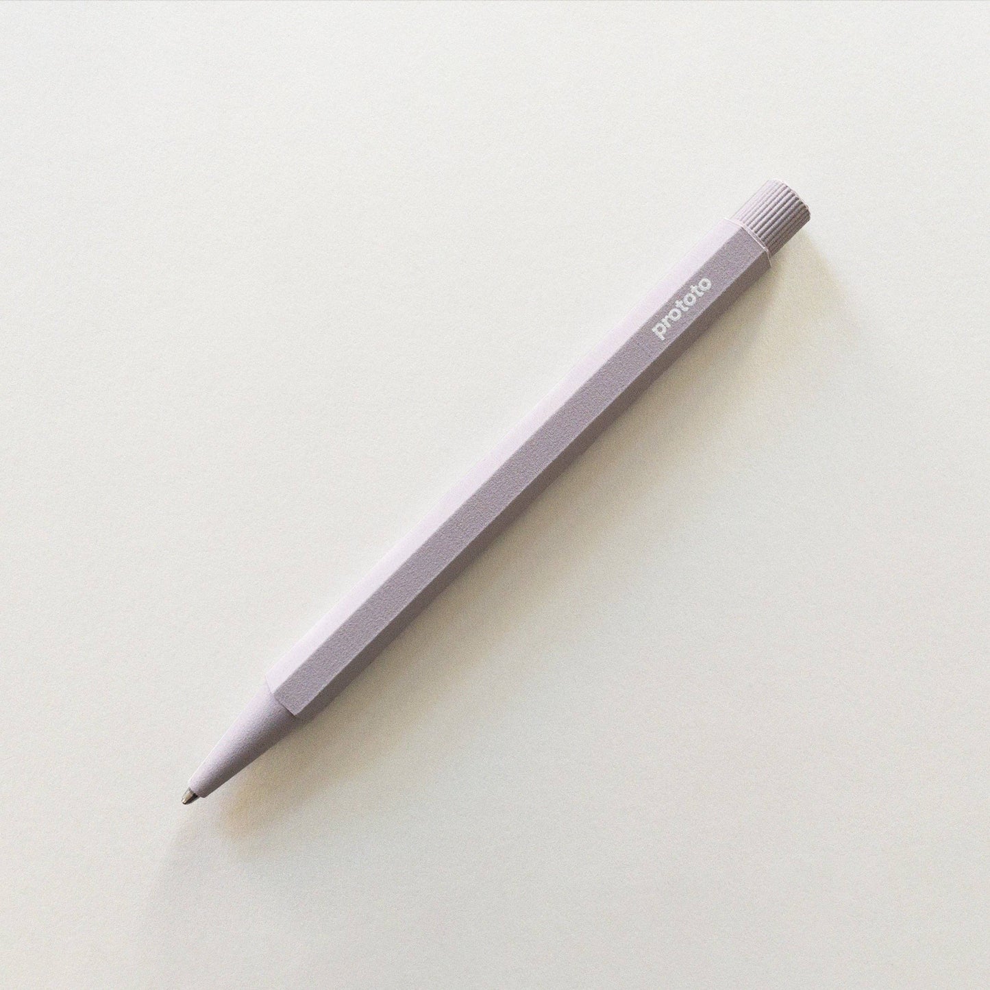 Ein lavendelfarbener Prototo - Zero Waste Kugelschreiber von Prototo aus recycelbaren Materialien mit sechseckigem Korpus und dem Logo im oberen Bereich liegt diagonal auf einer schlichten weißen Fläche und verbindet Stil mit nachhaltigem Design.