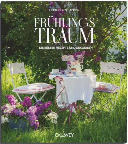 Ein Buchcover zeigt einen Garten mit einem kleinen Tisch, zwei weißen Stühlen, Flieder und einem Teeservice. Der Titel "Frühlingstraum" aus dem Callwey Verlag zeigt üppiges Grün und charmante Deko-Ideen, die an echte Frühlingsgefühle erinnern.