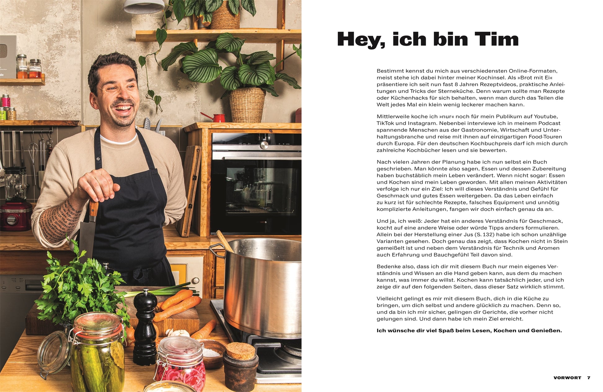Ein lächelnder Mann in einer Schürze steht in einer gemütlichen Küche mit frischem Gemüse und Küchenutensilien – eine einladende Szene für „Mach‘s lecker!“ Kochkurs und Rezepte des DK Verlags.