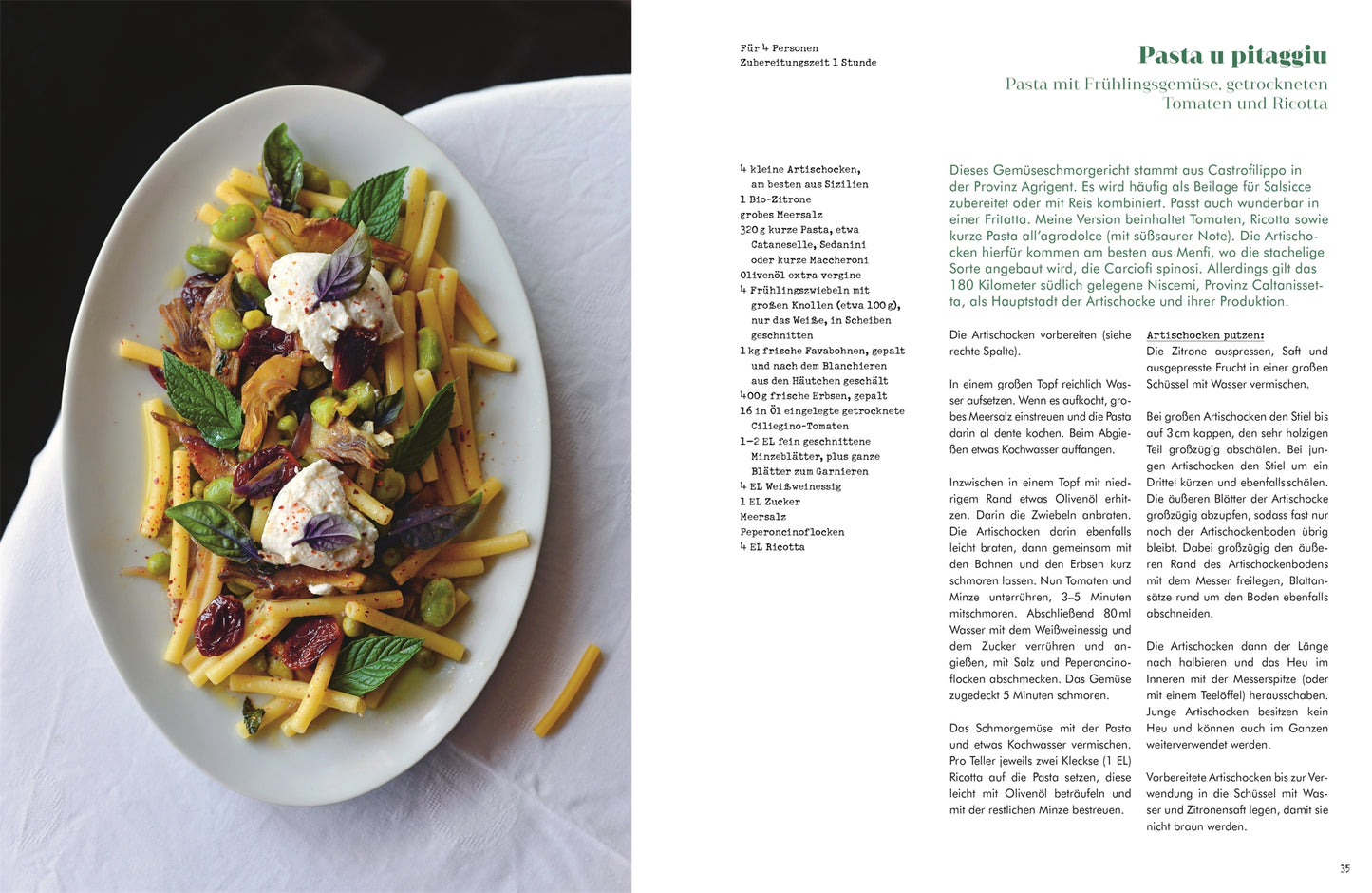 Auf einem dunklen Tisch steht ein weißer ovaler Teller mit gelben Nudeln, sonnengetrockneten Tomaten, Ricotta, Pistazien und Minze; auf der Seite daneben ist ein authentisches sizilianisches Rezept aus "Sizilien in meiner Küche" vom DK Verlag auf Deutsch abgebildet.