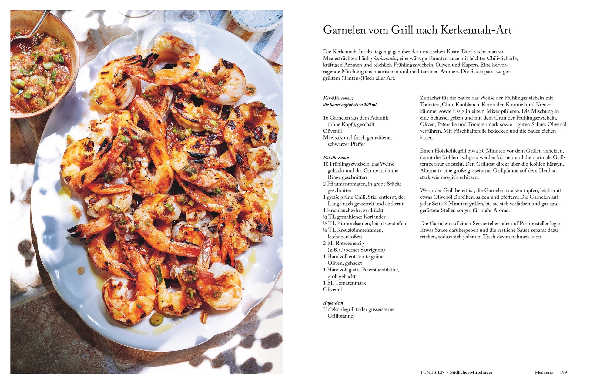 Eine weiße Platte mit gegrillten Garnelen aus dem DK Verlag Mediterra steht mit Kräutern und Zitrone garniert auf einem sonnenbeschienenen Tisch neben Wasser und einem Rezept für Garnelen vom Grill nach Kerkennah-Art.