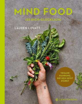 Eine Hand hält frische Kräuter und Gemüse vor einem grauen Hintergrund. Oben ist der Buchtitel "Mind Food - Iss dich glücklich!" aus dem Gerstenberg Verlag abgebildet, der in einem gelben Kreis die vegane Ernährung für Ihr emotionales Wohlbefinden hervorhebt.