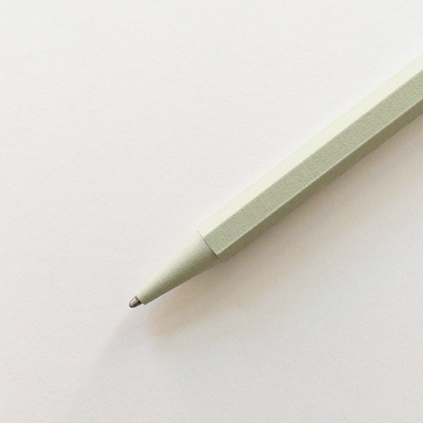 Eine Nahaufnahme des Prototo – Zero Waste Kugelschreibers in Salbei von Prototo, einem klimaneutralen, hellgrünen Stift mit sechseckigem Korpus, diagonal auf weißem Untergrund abgebildet.