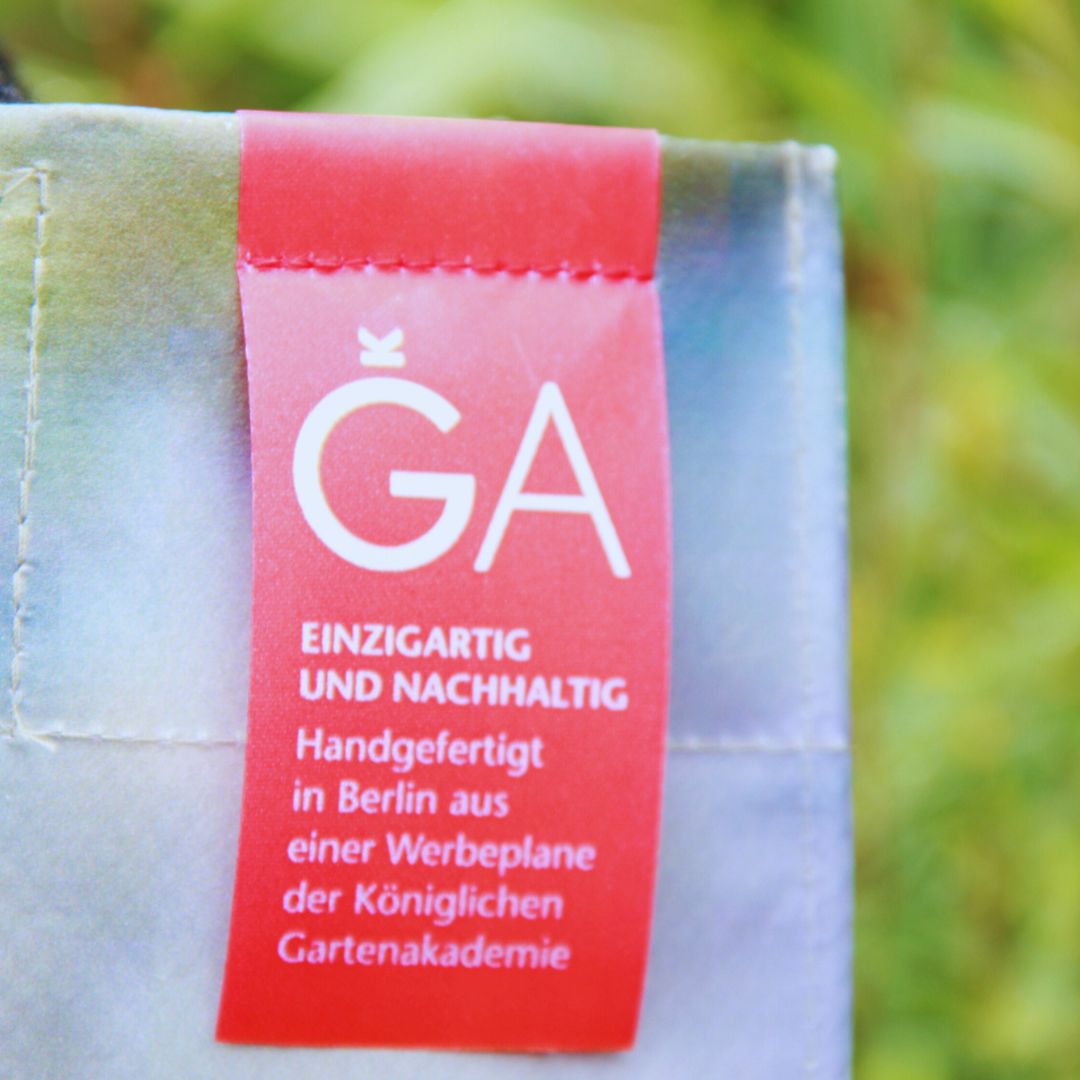 Eine Nahaufnahme eines roten Stoffetiketts mit weißem Text auf dem Upcycling KGA Shopper "Leaf" der Königlichen Gartenakademie - eine nachhaltige Tasche, die in Berlin aus recycelten Werbebannern handgefertigt wurde.