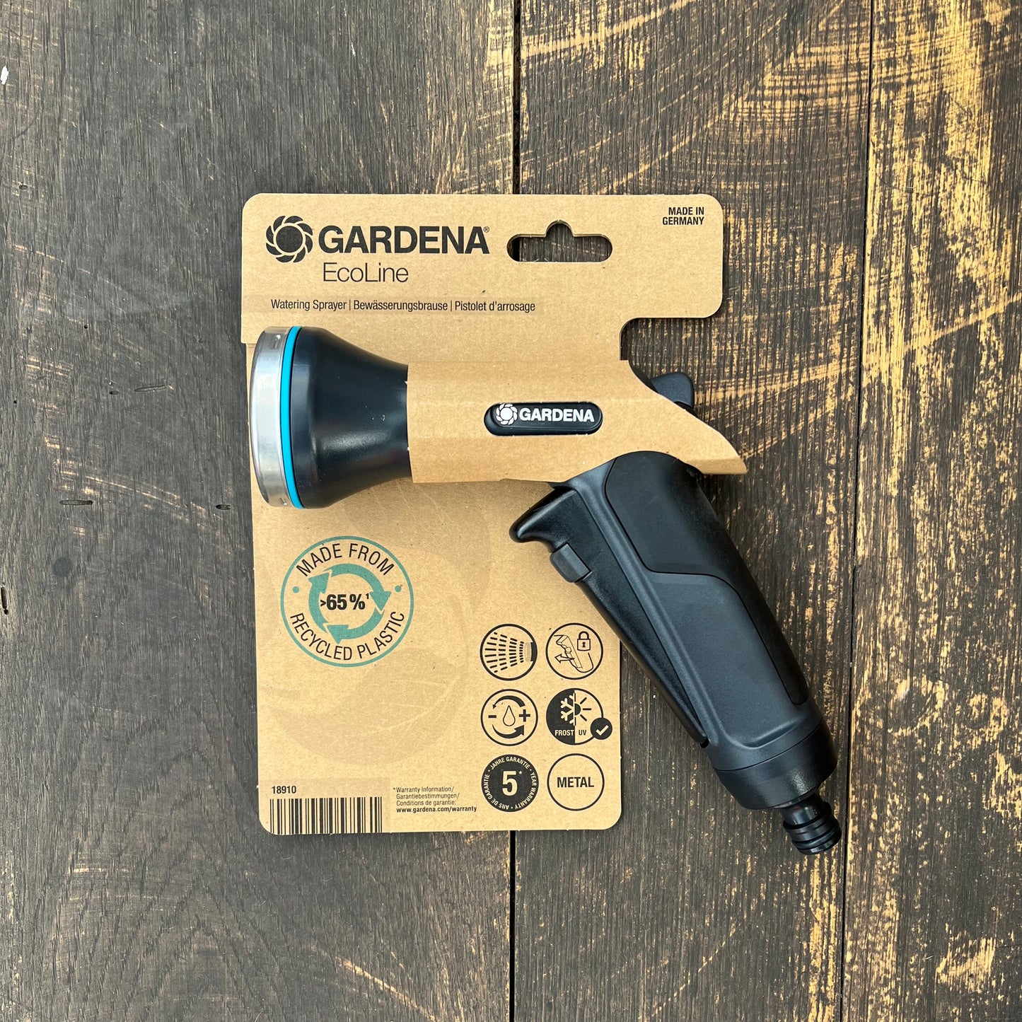 Die Gardena Eco Line Bewässerungsbrause von Gardena besteht zu 65% aus recyceltem Kunststoff, kommt in brauner Verpackung und bietet nachhaltige Gartenbewässerung - ideal präsentiert auf rustikalem Holz.