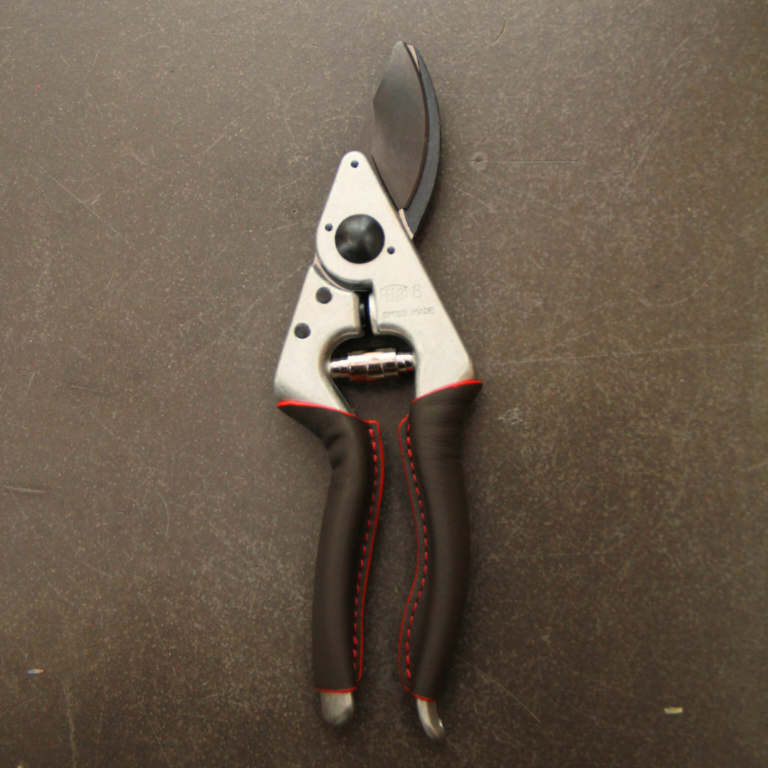Ein Paar Felco 8 ELITE Gartenscheren von Felco mit schwarzen Klingen und Griffen mit roten Nähten ruht auf einer dunklen, strukturierten Oberfläche.