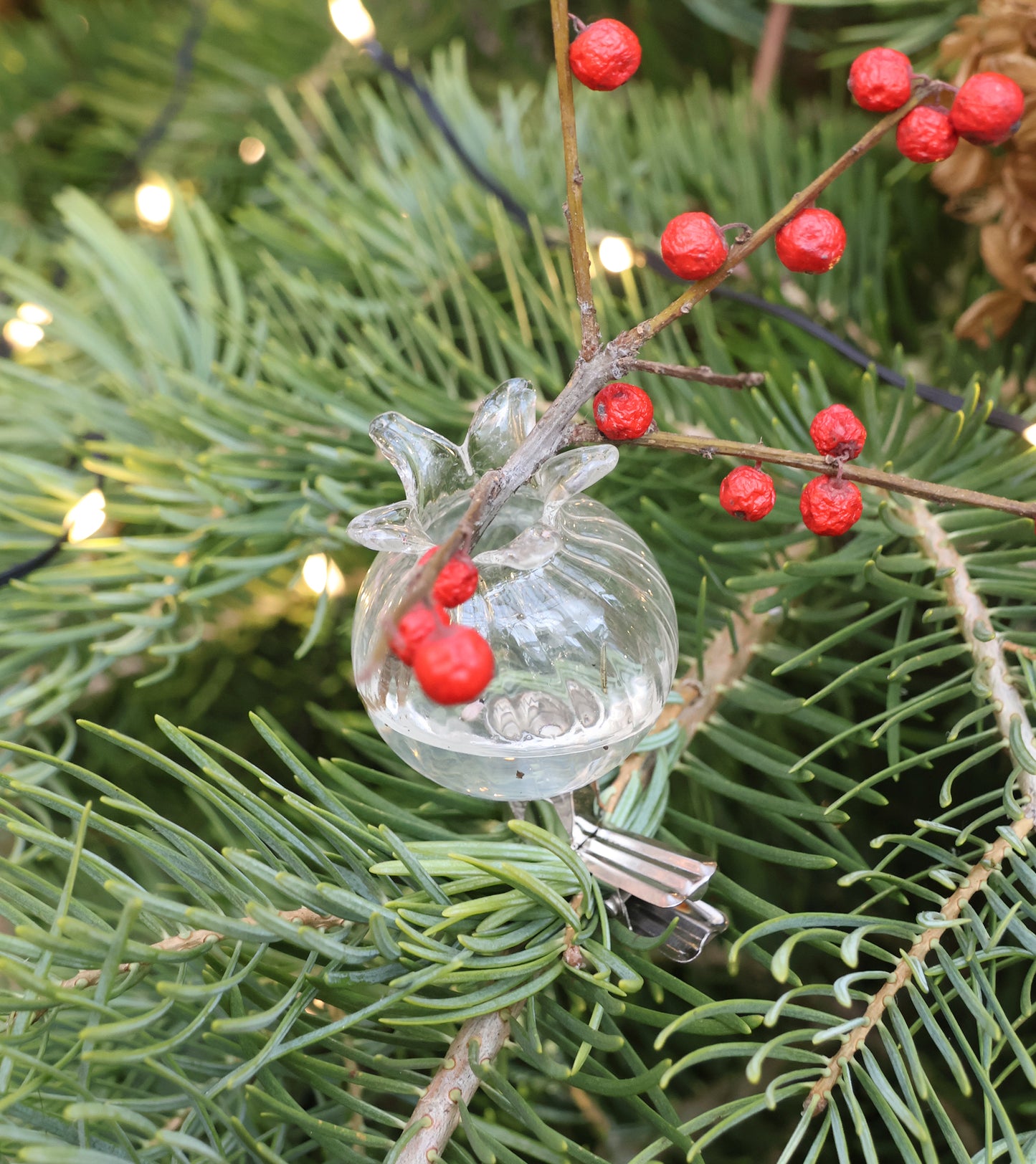 Das Klemmvasen | 6er Set der Königlichen Gartenakademie besteht aus gläsernen Minivasen in Granatapfelbauform, die sich an den Zweigen befestigen lassen und mit kleinen roten Beeren, Tannennadeln und Lichterketten dekoriert werden können.