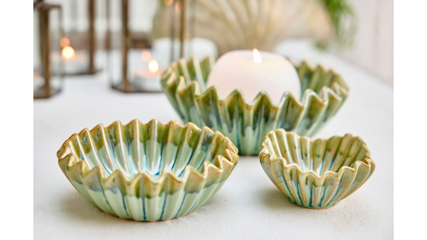 Die kleine grüne Schale 'Wave' von 2 Have (5 x 10 cm) mit welligem Rand präsentiert sich auf weißem Untergrund, eine weiße Kerze darin - sanftes Kerzenlicht schimmert im Hintergrund.
