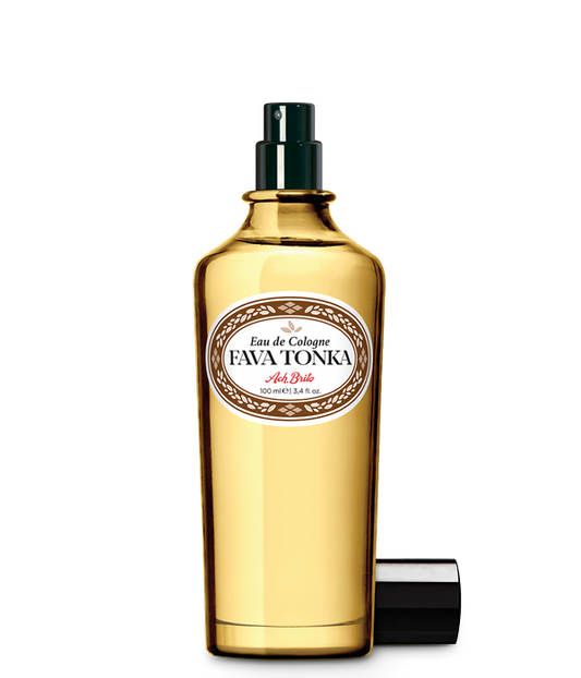 Der goldgelbe Glasflakon von Ach.Brito - Eau de Cologne - Fava Tonka 100 ml hat einen schwarzen Sprühkopf, ein weißes Etikett mit dunkler Schrift und eine Kappe daneben, die den einzigartigen Tonkabohnen-Duft dieses Ach.Brito-Duftes hervorhebt.