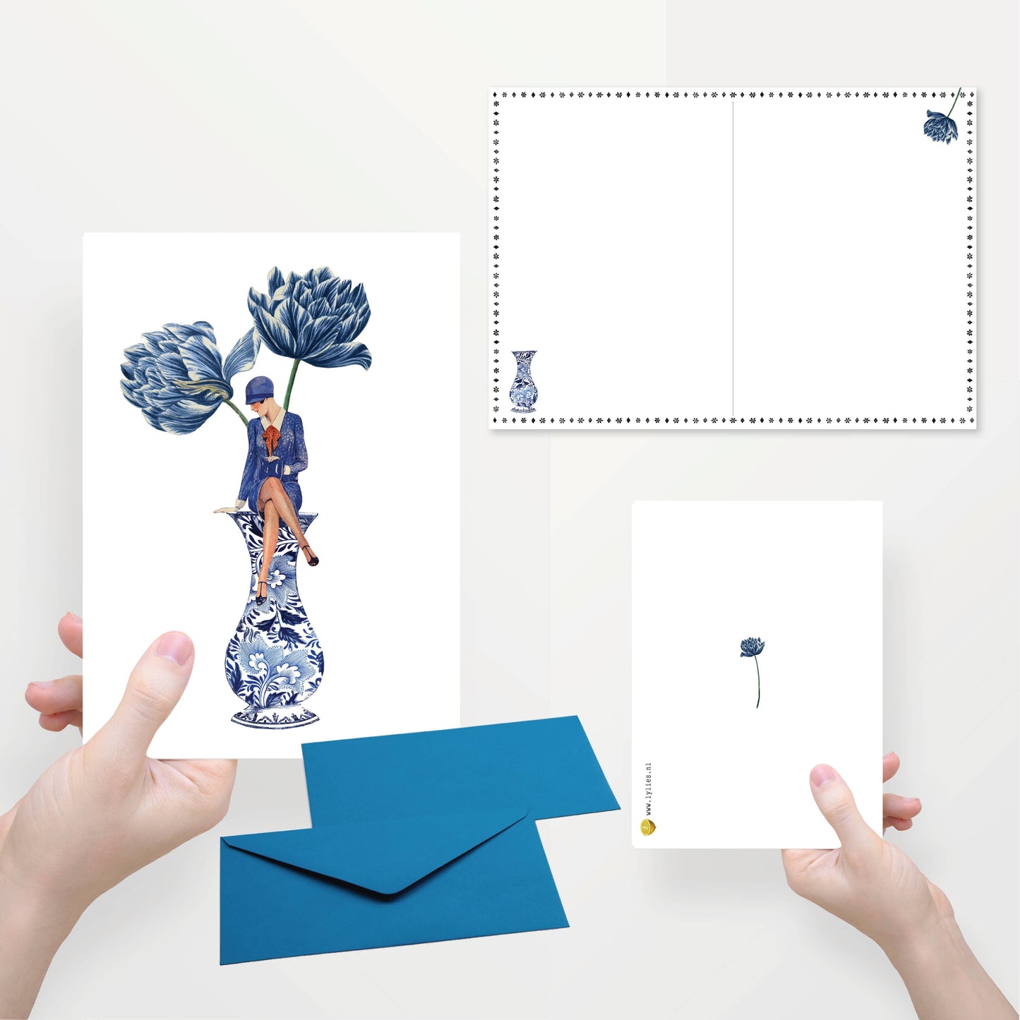 Eine Person hält die Lylies - Zur Hälfte gefaltete Grußkarte mit einem Damenumschlag auf einer blauen Vase. Eine andere Hand zeigt eine kleinere Karte mit einer blauen Blume. Blaue Umschläge und Kartenrückseiten aus Recyclingpapier sind sichtbar.