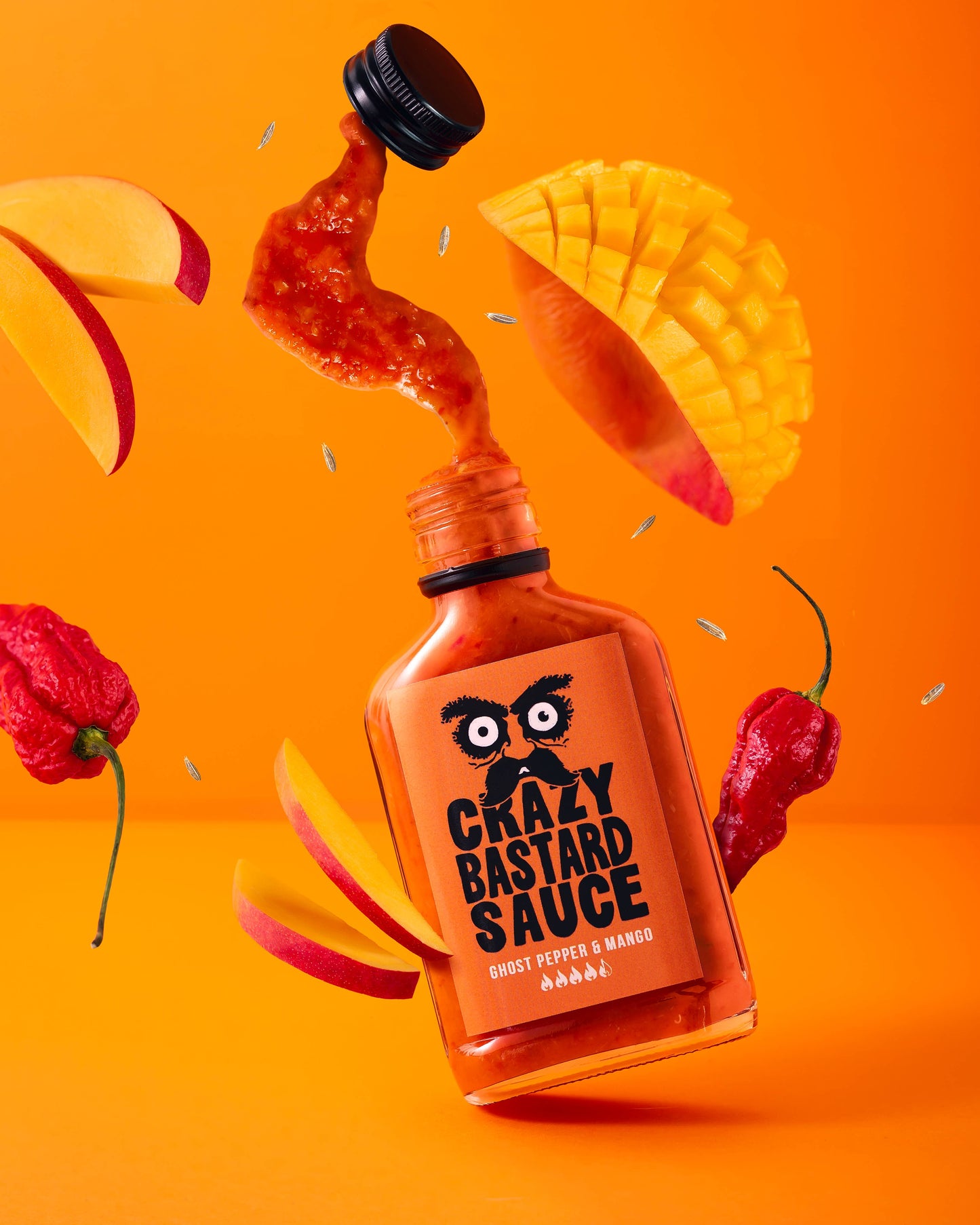 Eine 100-ml-Flasche CBS Foods GmbH (Crazy Bastard Sauce) - Geisterpfeffer & Mango scharfe Soße ist umgeben von geschnittener Mango, saftigen Mangostücken, Geisterpfeffer und Spritzern der scharfen Soße auf einem leuchtend orangen Hintergrund.