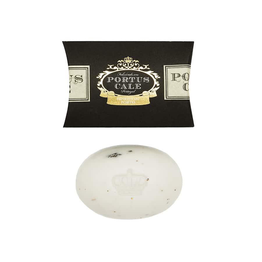 Die weiße, ovale Seife Portus Cale 40 g - Ruby Red von Castelbel weist dezente braune Flecken auf und ruht unter ihrer eleganten schwarz-goldenen Verpackung. Diese luxuriöse Duftseife ist auf pflanzlicher Basis hergestellt für eine sanfte, raffinierte Reinigung.