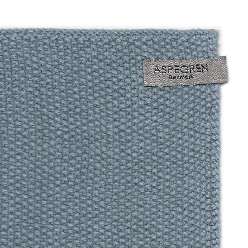 Eine Nahaufnahme eines strukturierten, hellblauen Aspegren Denmark Spültücher, gestrickt und einfarbig, aus Baumwolle mit grauem Label in der Ecke, das „Aspegren Denmark“ zeigt.