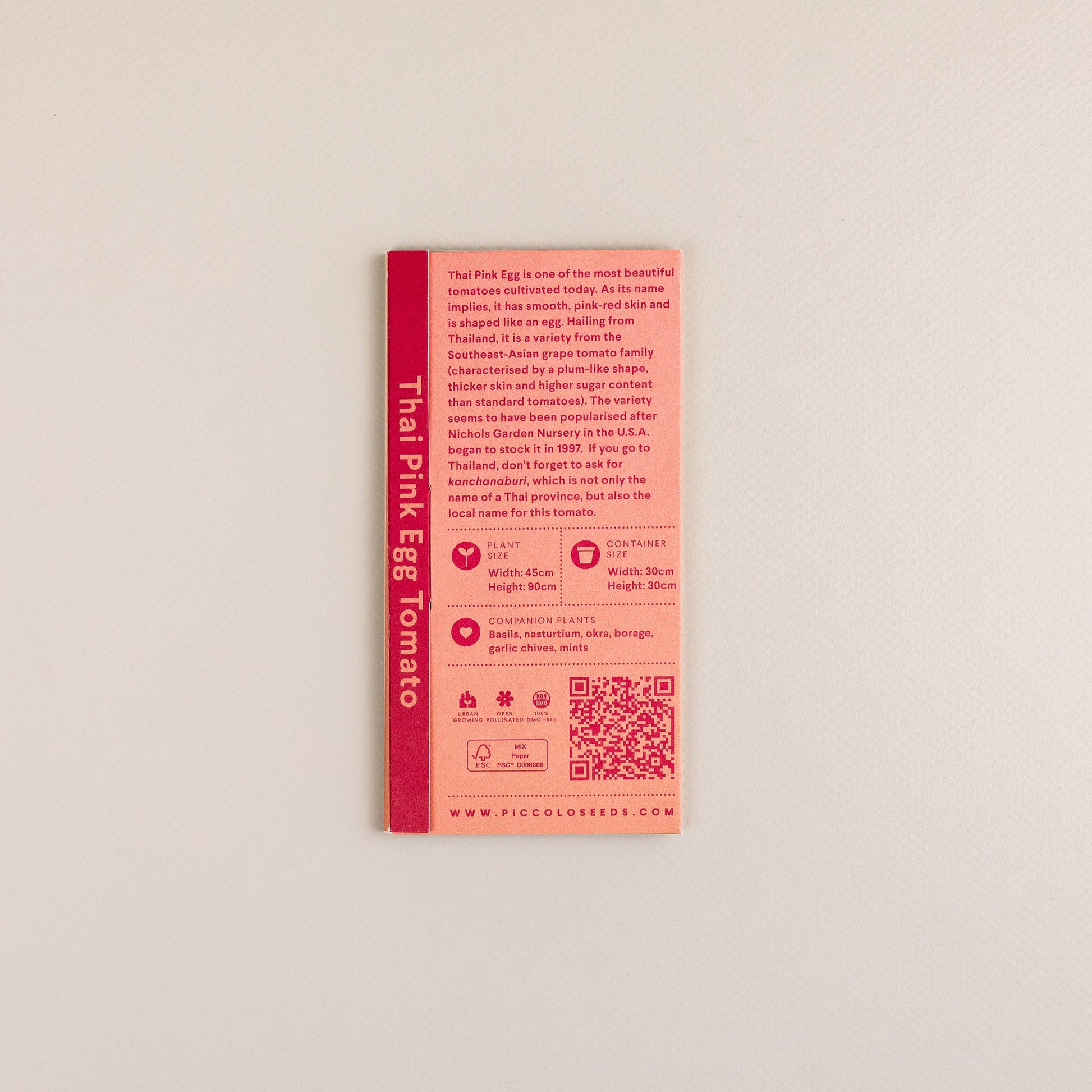 Eine Saatgutpackung mit der Aufschrift Piccolo Seeds - Tomaten-Thai-rosa Ei enthält Text und Symbole zu dieser südostasiatischen Tomatensorte, Pflanzinformationen und einen QR-Code, alles auf einem schlichten weißen Hintergrund. Marke: Piccolo Seeds.