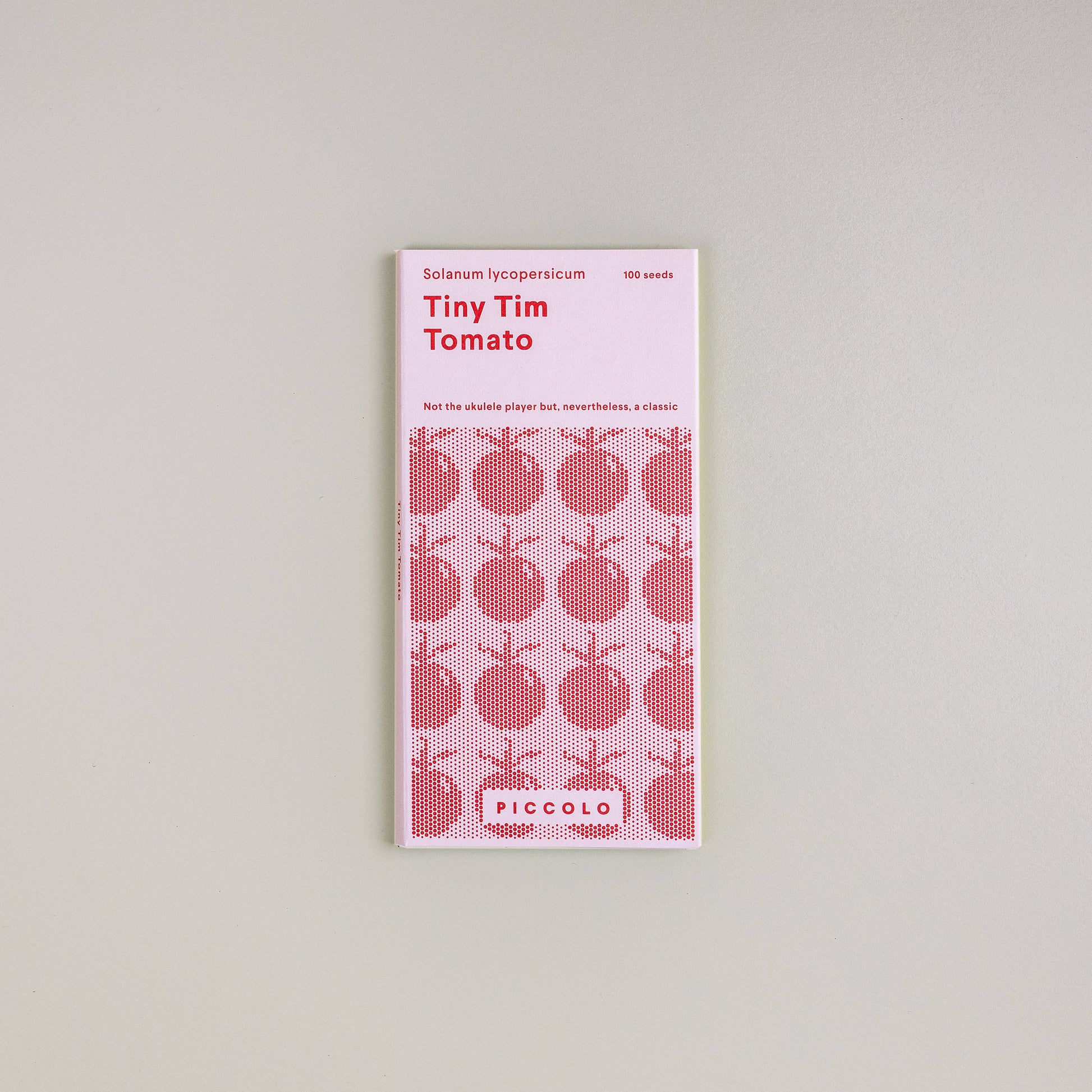 Eine Packung Piccolo Seeds - Tomate Tiny Tim von Piccolo Seeds, ideal für kompakte Tomaten oder Zwergtomaten, ist auf einem schlichten Hintergrund abgebildet. Die rot-weiße Packung zeigt Tomatenabbildungen und gibt an, dass sie 100 Samen enthält.